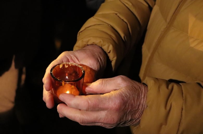 A man holds a small candle in an orange glass container