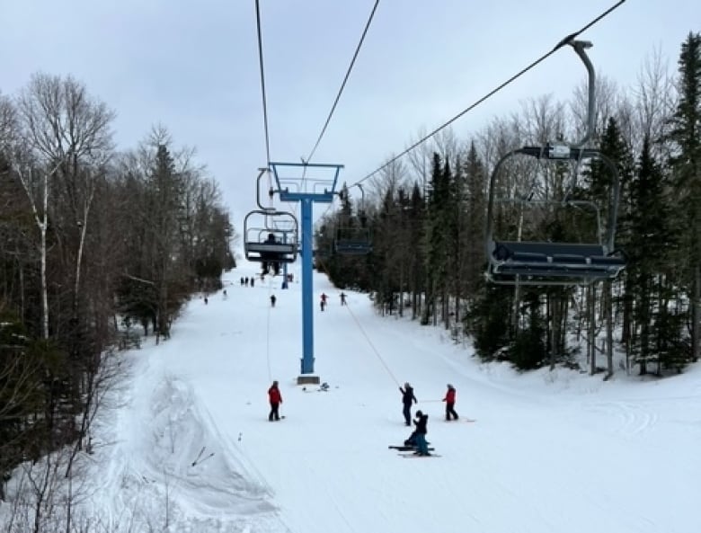 A photo of a ski hill's chair lift, with various teams of people on the ground holding ropes.
