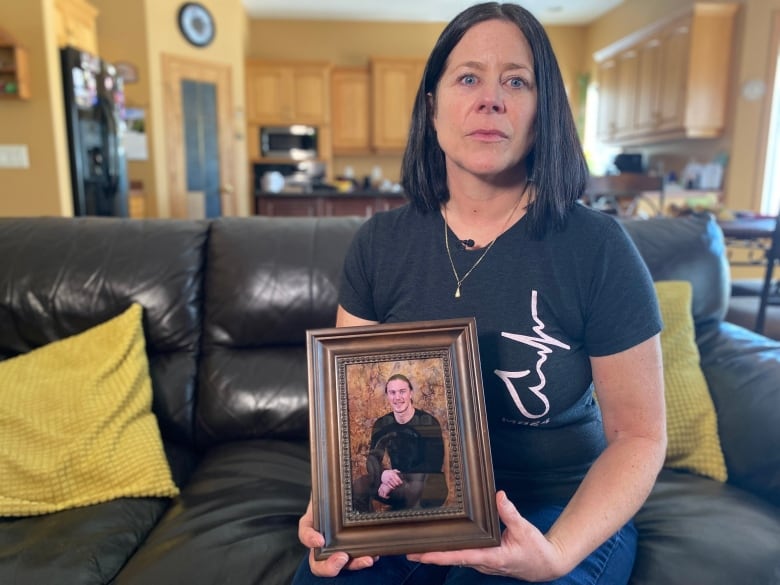 Shari Baraniuk sits on her couch and holds a framed photo of her son.