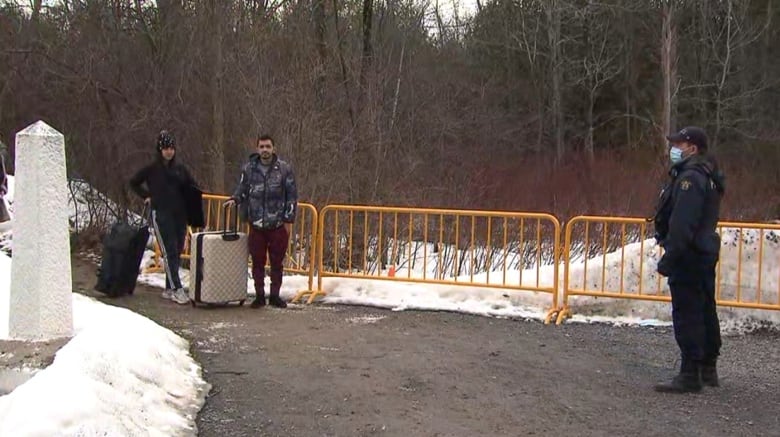 A Venezuelan couple stand on the U.S. side of Roxham Road while an RCMP on the Canadian side looks at them. 