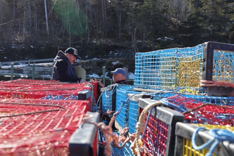 Two men talk among brightly coloured lobster traps in the foreground.