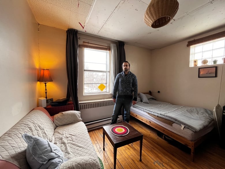 A man stands inside his small studio apartment.