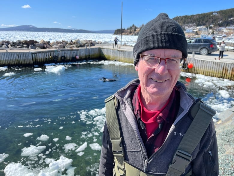 A man in a toque with icy water and dolphins in background
