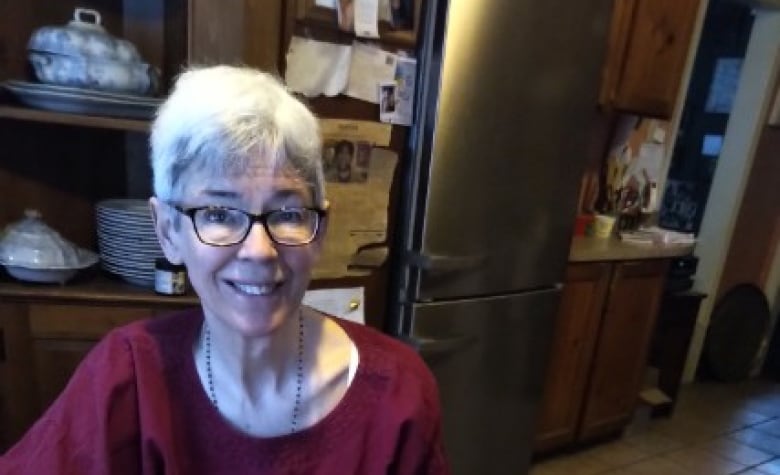 A woman sitting at a table in a kitchen smiles at the camera. 