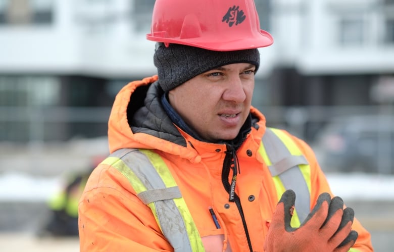A man in a hard-hat and cold-weather work clothing smiles at the camera on a construction site.