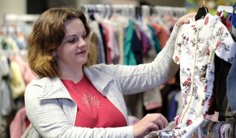 A woman examines a piece of children's clothing while standing in the clothing section of a donation centre.
