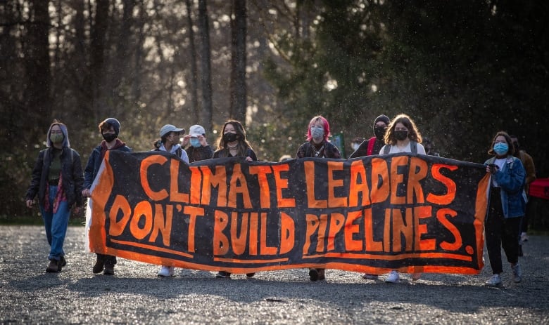 Protesters hold a black banner with orange letters that reads: 'Climate Leaders Don't Build Pipelines.'