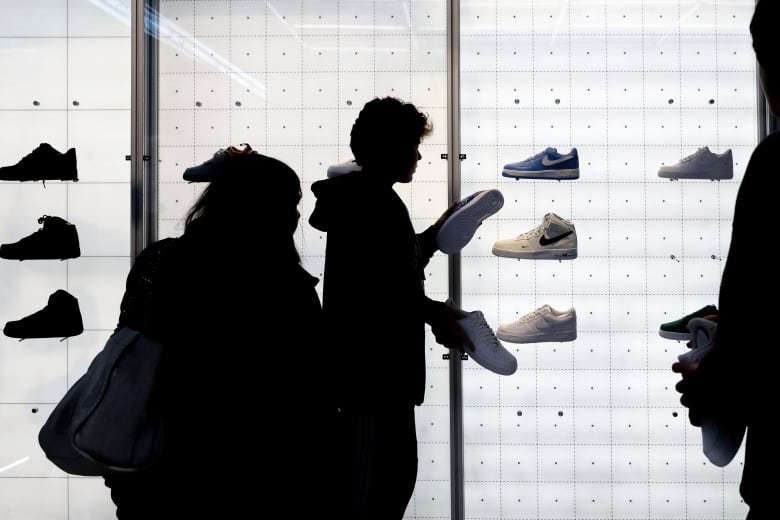 People in silhouette shop against an illuminated wall of shoes. 