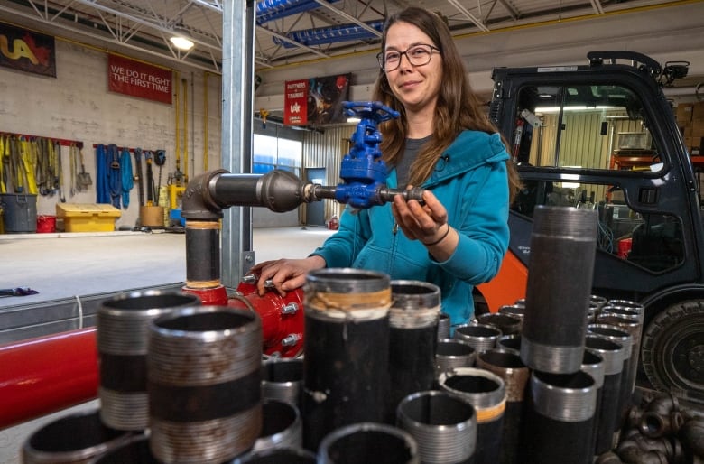 A woman smiles from behind a cart of pipefitting equipment in a training facility. 