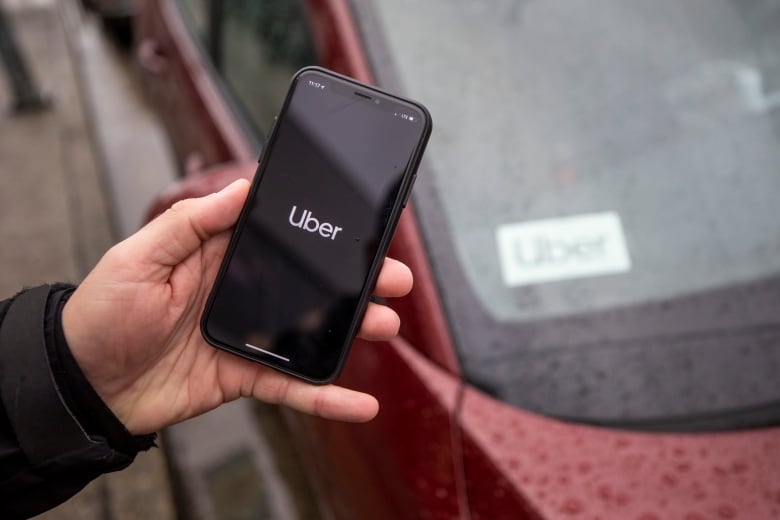 A person holds up an phone with 'Uber' on it, with a car in the background having an 'Uber' label on the dash.