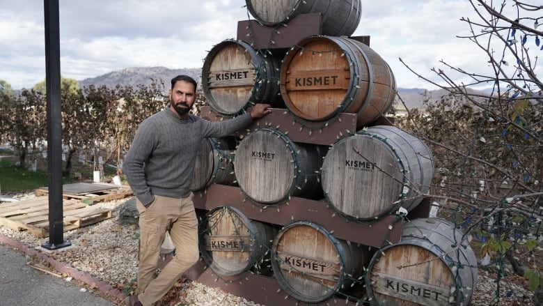 A man wearing stands next to a stacked pyramid of wine barrels at Kismet Estate winery in Oliver, B.C. 