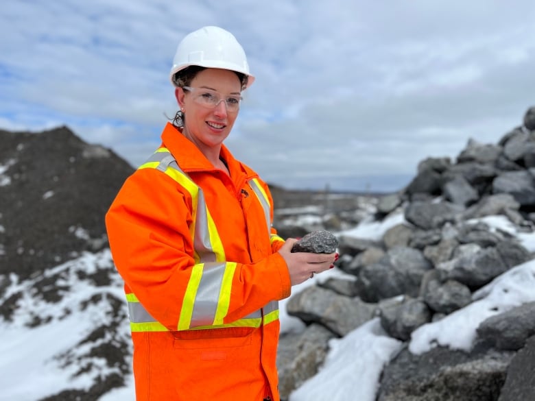 A woman wearing a hardhat and vest holds a rock.