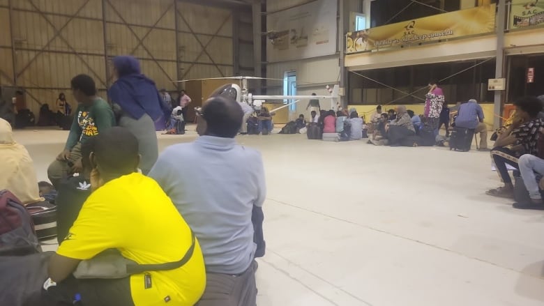 People wait at a Sudanese military airport for a rescue flight to arrive.