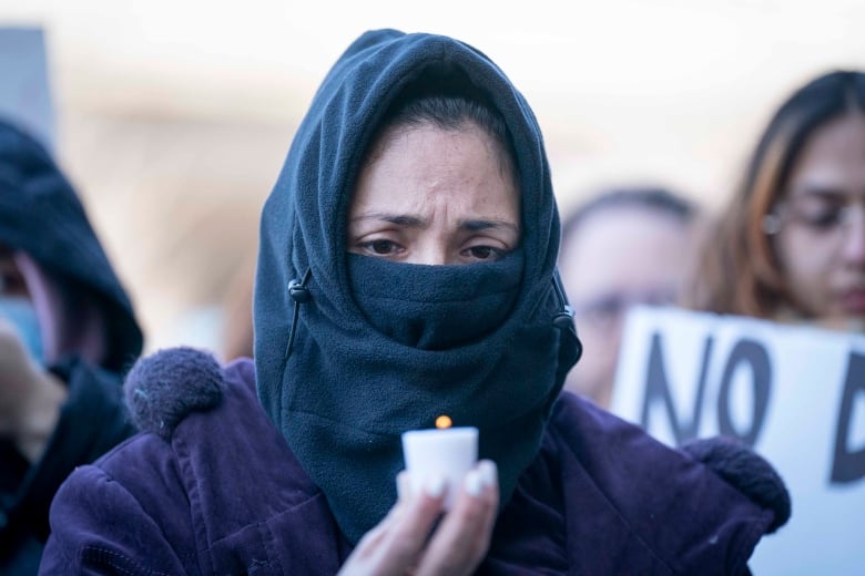 A woman hearing a black polar balaklava holds a candle at the protest outside Trudeau's Montreal riding office.