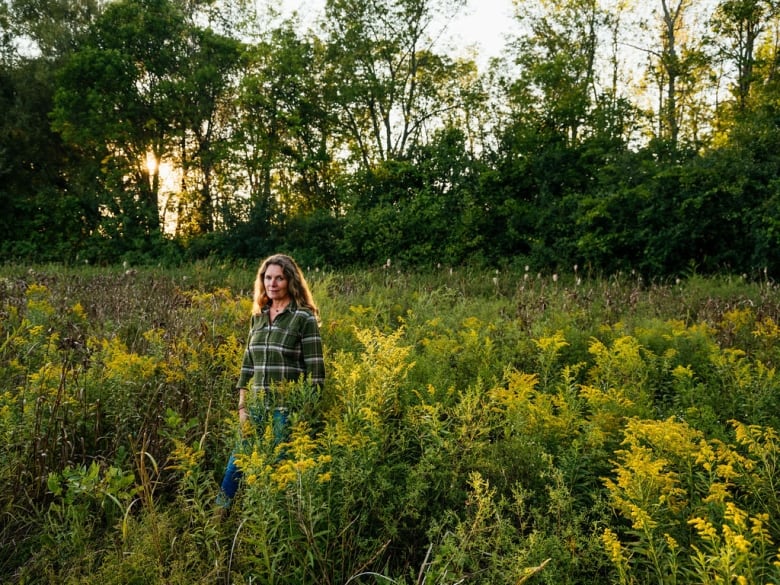 Woman stands in a meadow of waist-high plants. 