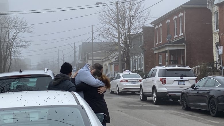 People hug near parked cars. It is misty outside