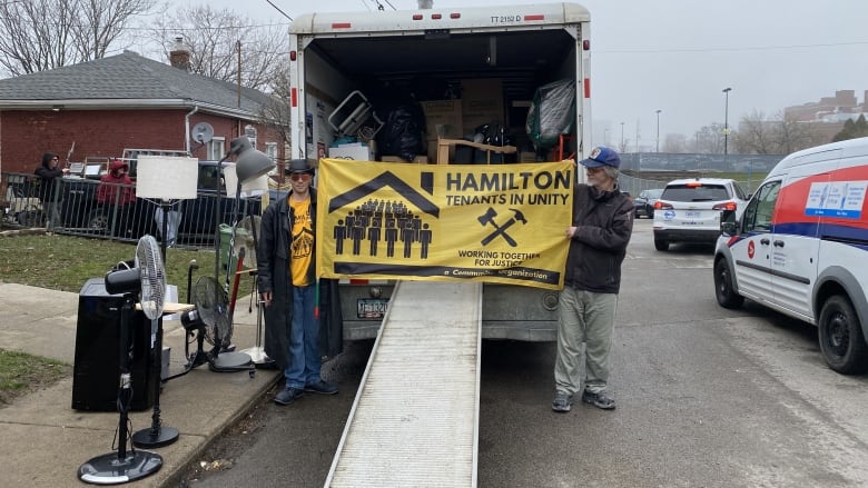 Two people hold a yellow banner in front of a truck