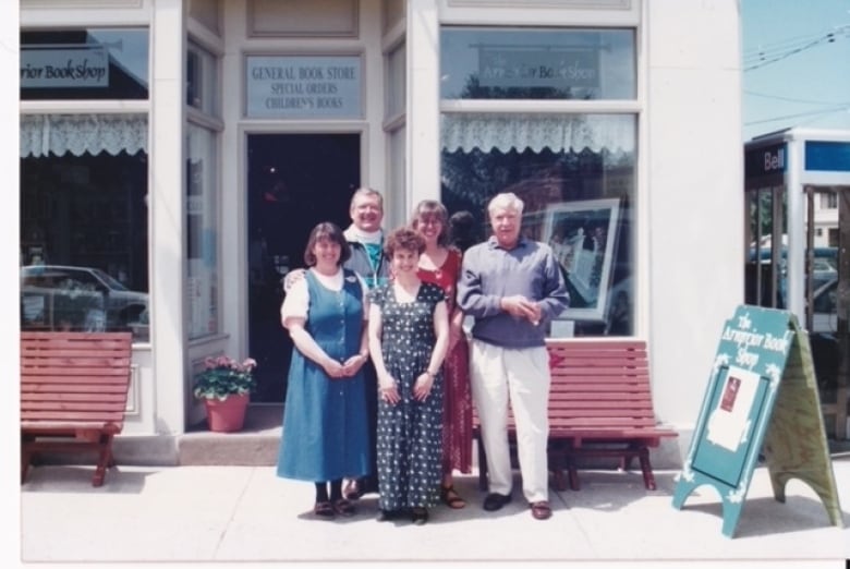 A group of five people standing on the sidewalk in front of a bookstore. 