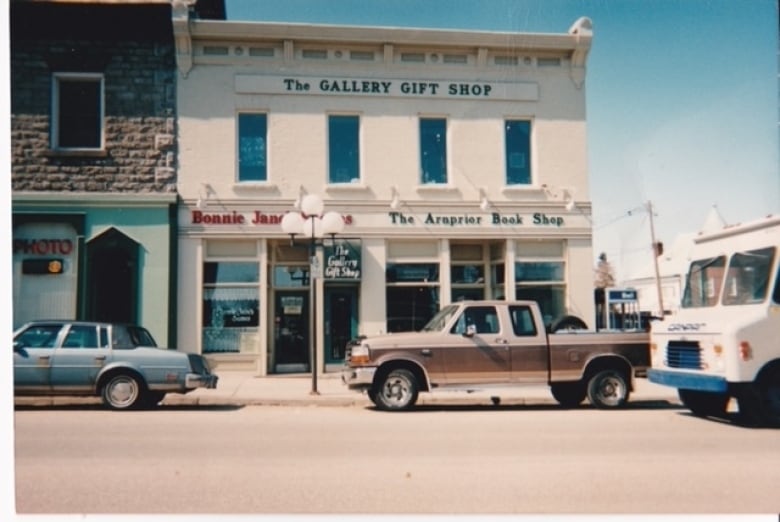 The outside of a storefront with trucks and a few cars seen passing by. 