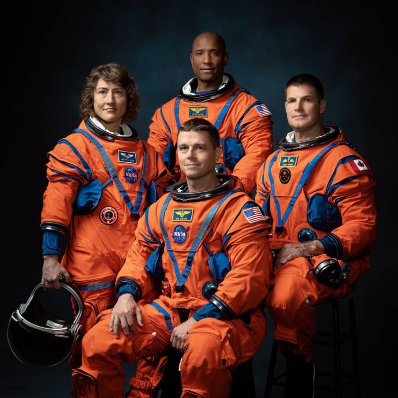 Four people, a woman and three men, pose in orange space suits.
