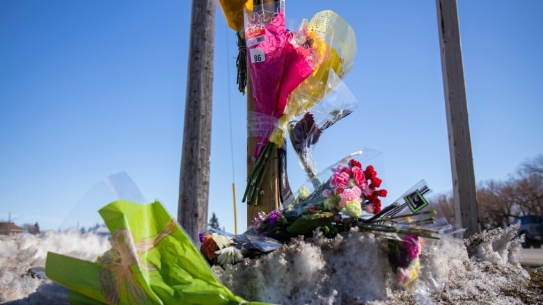 A close-up of a makeshift roadside memorial with flowers set on the ground.