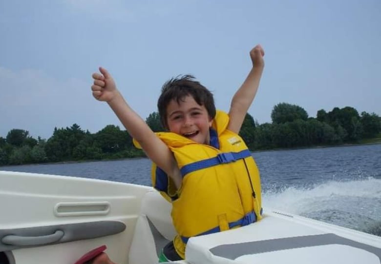 Harrison raises his arms in the air on a speed boat with a smile on his face. 