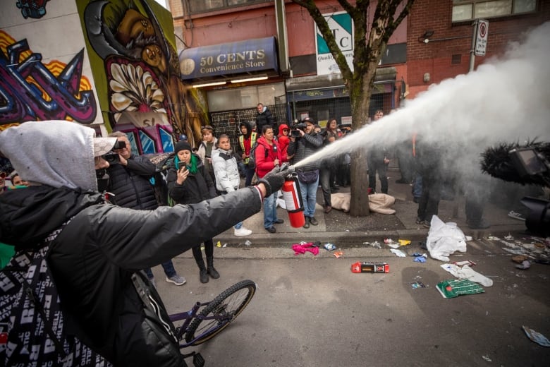 A man sets off a fire extinguisher on the streets, aiming it away