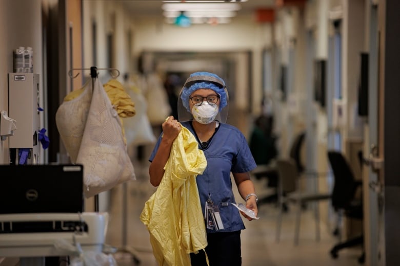 A nurse gowns up before attending to a patient in the intensive care unit of Humber River Hospital, in Toronto, on Jan. 25, 2022.