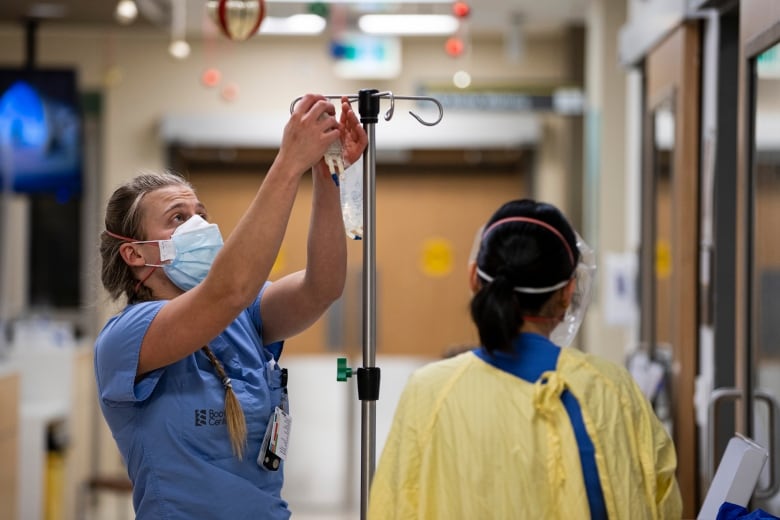A nurse readies a bag on a hospital stand for a patient.