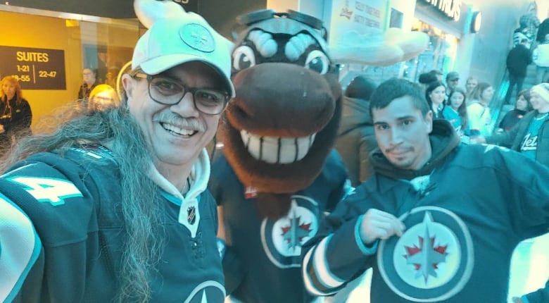Two men are pictured in Winnipeg Jets jerseys, posing with a mascot.