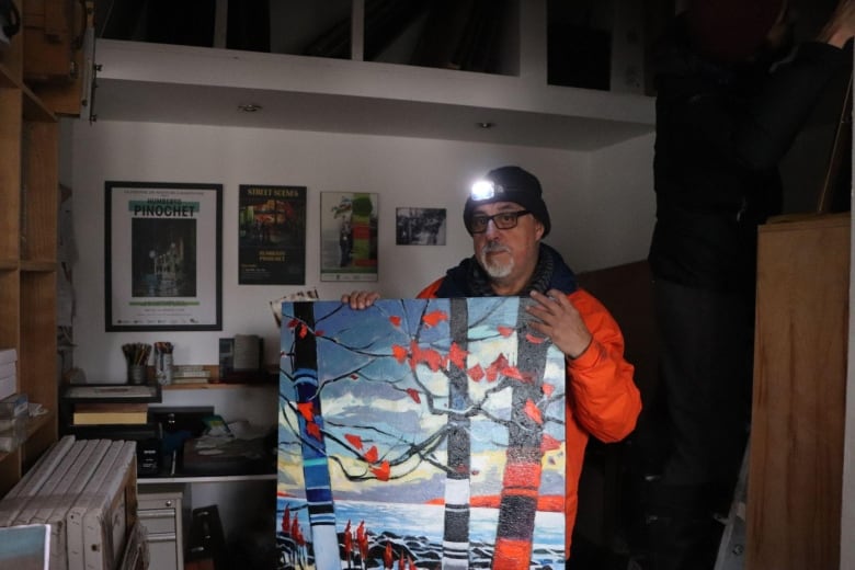 A man holds his painting wearing a headlamp 