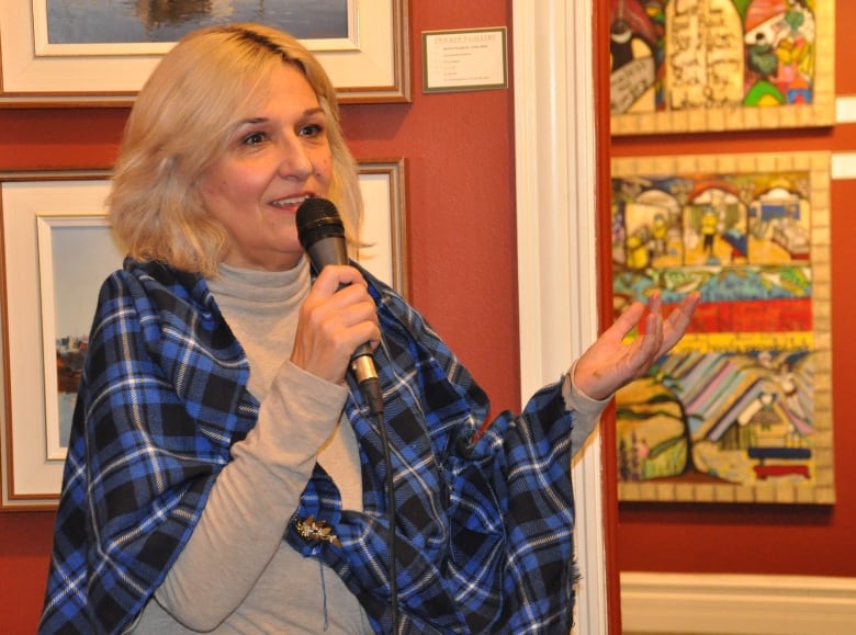 A woman holding a microphone speaks at the opening of her art exhibit.