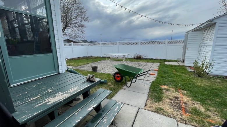 A wheelbarrow sits in a backyard. The overhead skies are grey. 
