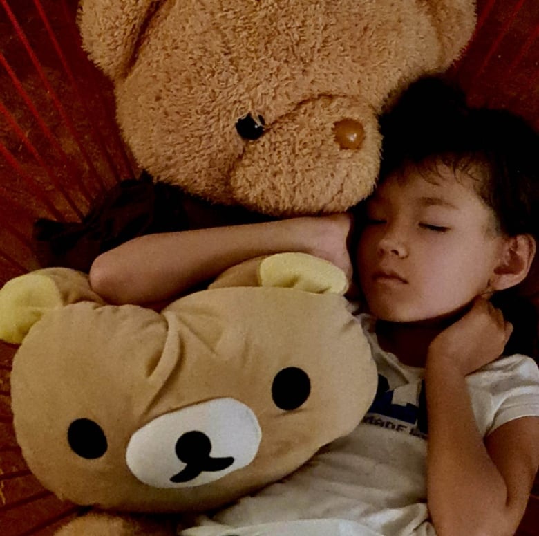 A girl sleeps with two extra-large teddy bears.