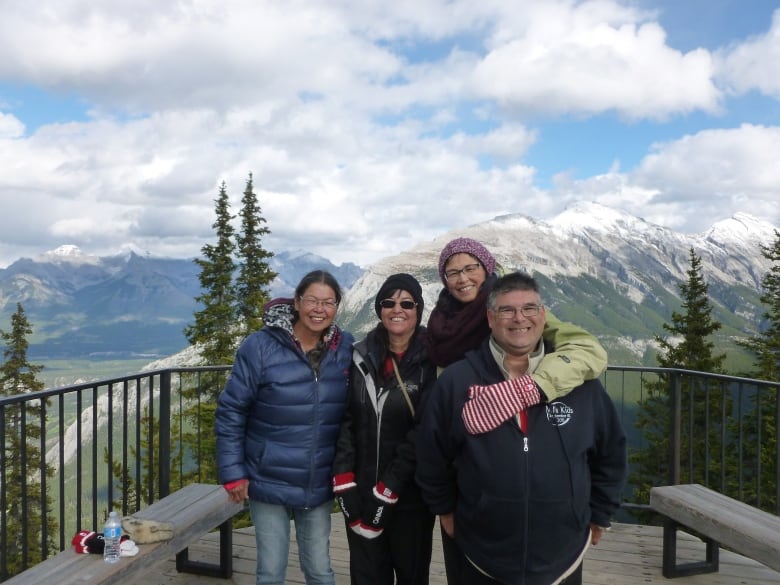 Three women and a man pose in front of a mountain view.