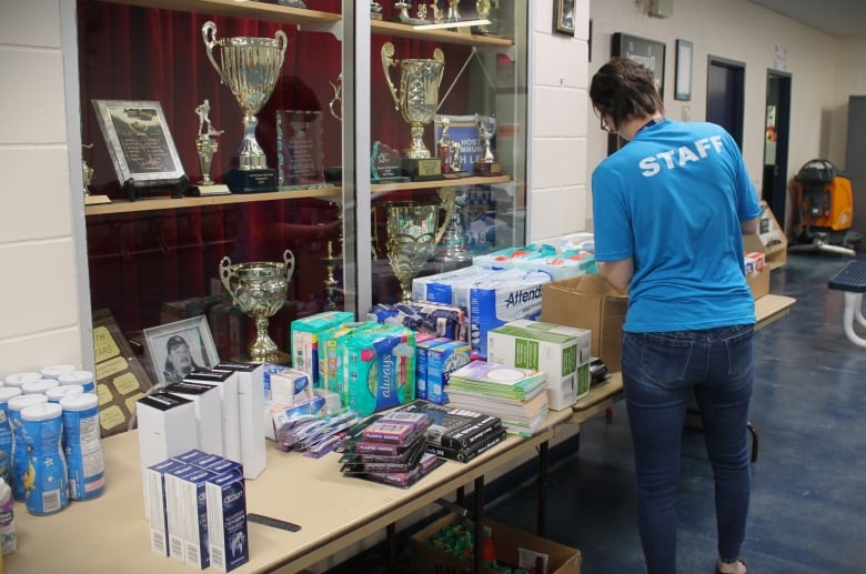 A volunteer with a blue shirt that says 'staff' standing by a table of supplies. 