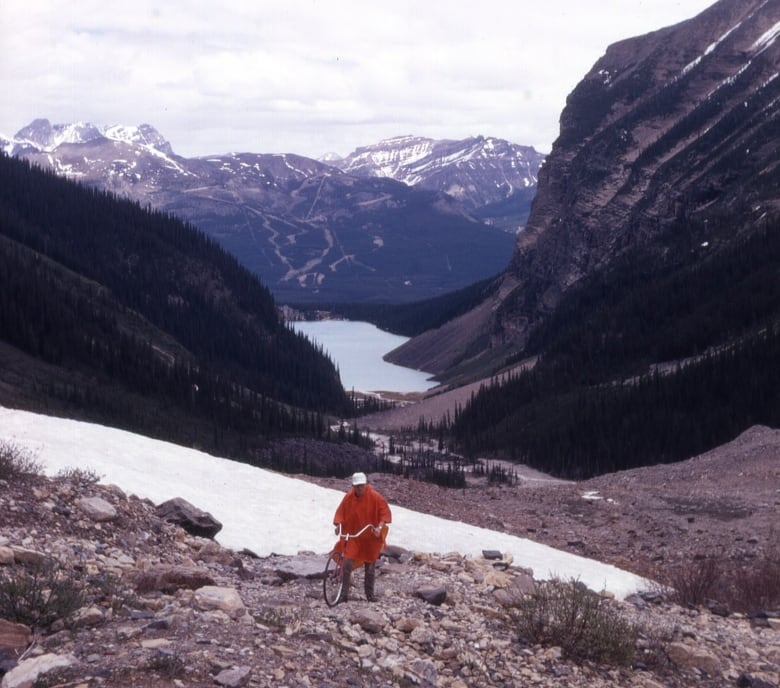 Brian Patton is pictured, poncho-ed and holding the trail wheel, while measuring the Plain of Six Glaciers trail in 1970.