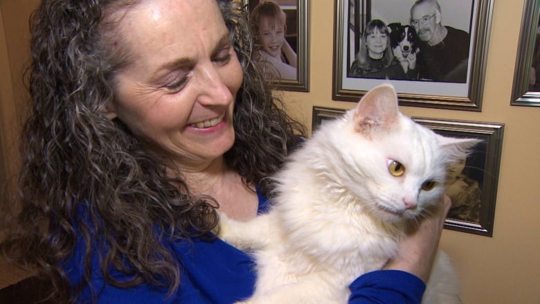 A smiling woman holds a white cat. 