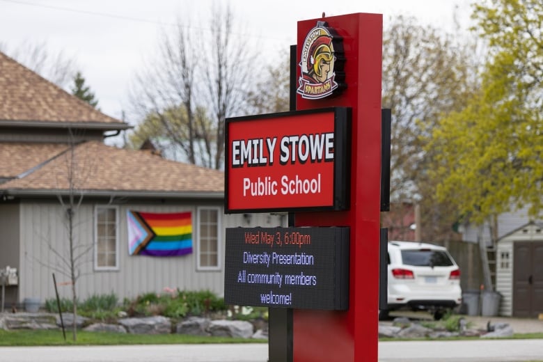 A pride flag is seen behind a school sign. 