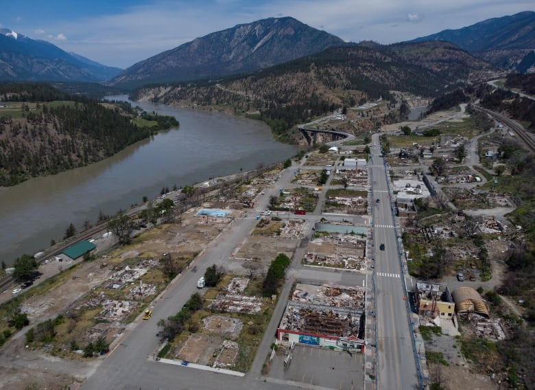 An overhead view of a town where most of the houses are destroyed, next to a river and mountains.