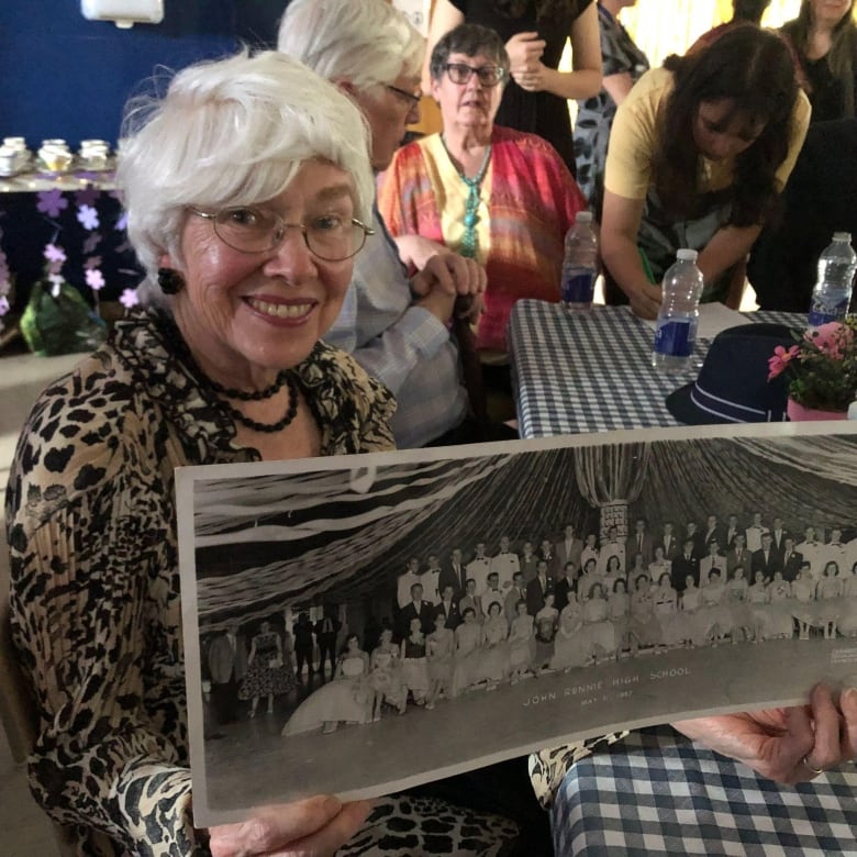 A woman holds up a black and white class photo