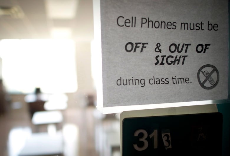 A photocopied signed taped to the door of a classroom reads: cell phones must be off & out of sight during class time. 