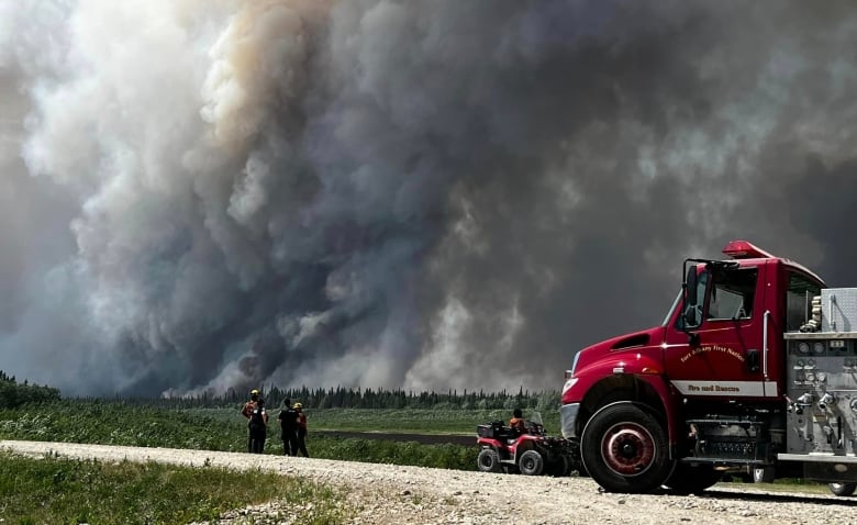 A fire truck is parked on a gravel road with a wall of smoke in the background