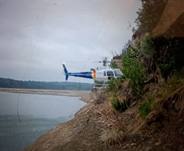 A helicopter approaches a steep embankment with water below. 