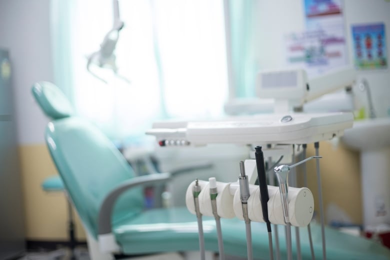 A stock photo shows dental instruments in the foreground with a light blue dentist's chair in a blurred background.