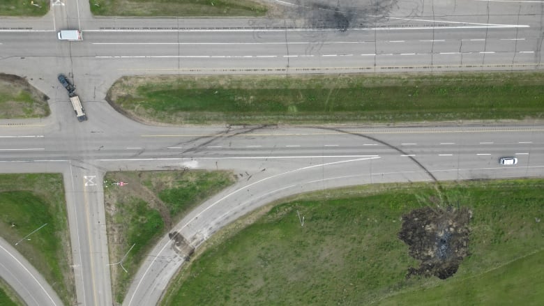 An overhead view of a highway intersection. Several vehicles are on the road, and there are large skid and burn marks across the highway.