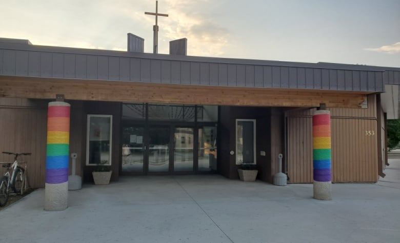 The exterior of a church with rainbow coloured ribbons taped along two columns by the entrance. 