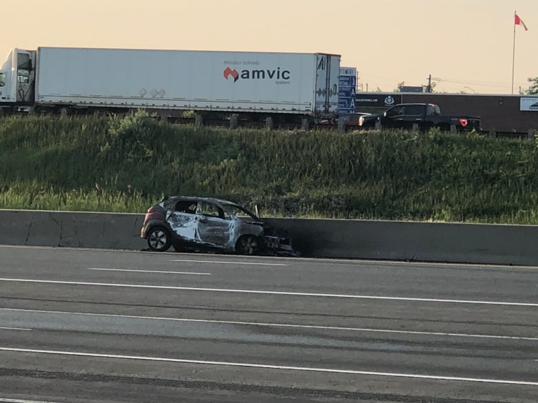 A burnt car on the shoulder of a highway