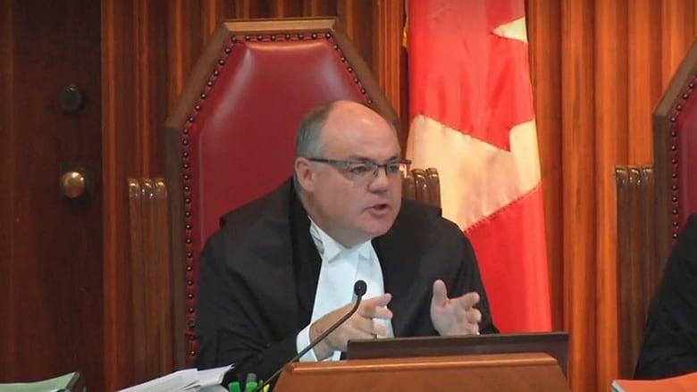 A judge sits in front of a Canadian flag.
