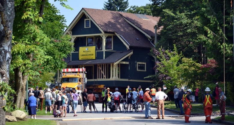 A photograph showing bystanders watch a blue heritage home on a truck roll down a residential street in Vancouver.